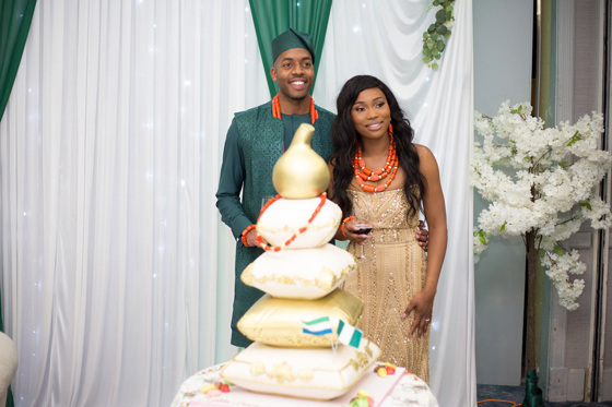 Bride and groom smile at guests behind traditional Nigerian pillow wedding cake